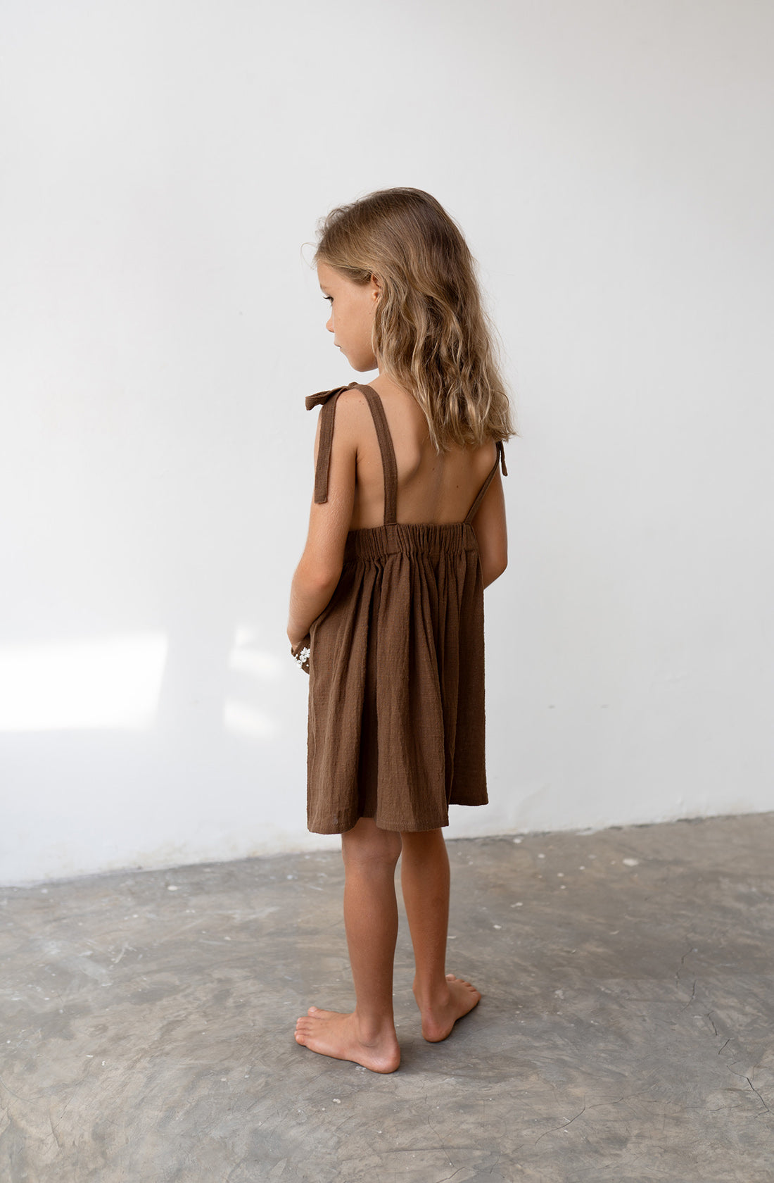 Young girl wearing the luna pinafore in cocoa.