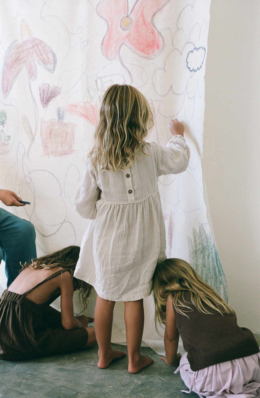 Young girl wearing the yumi dress in natural while drawing on a canvas.