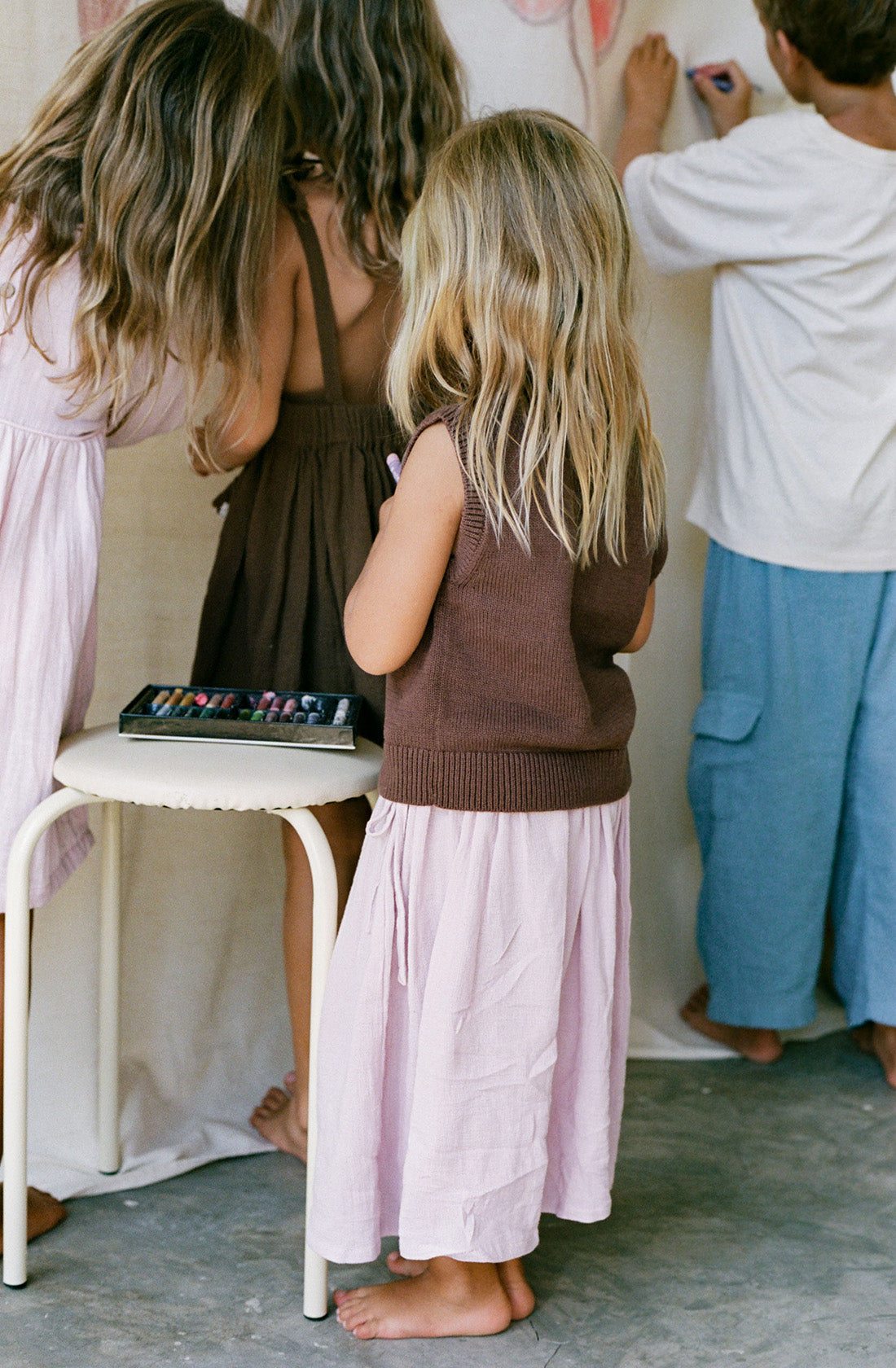 Young girl wearing the knit vest in cocoa and a pink skirt holding crayons.