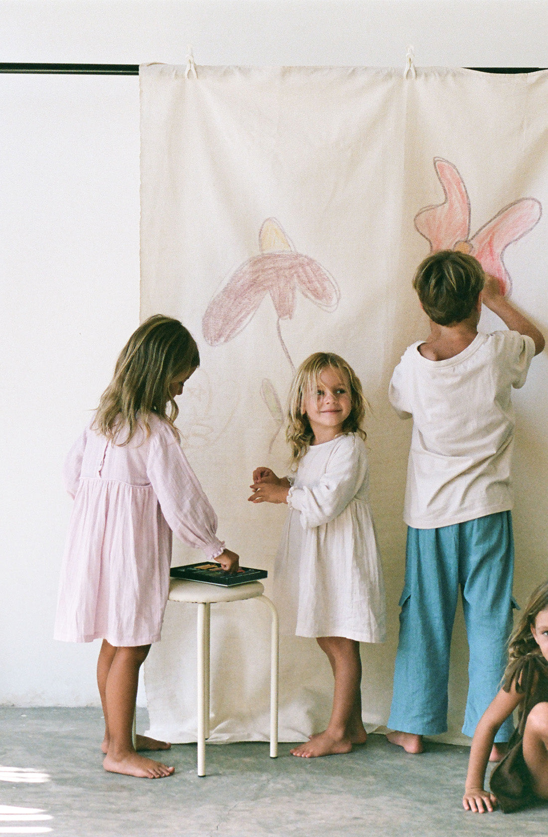 Young girl wearing the yumi dress in natural while drawing on a canvas.