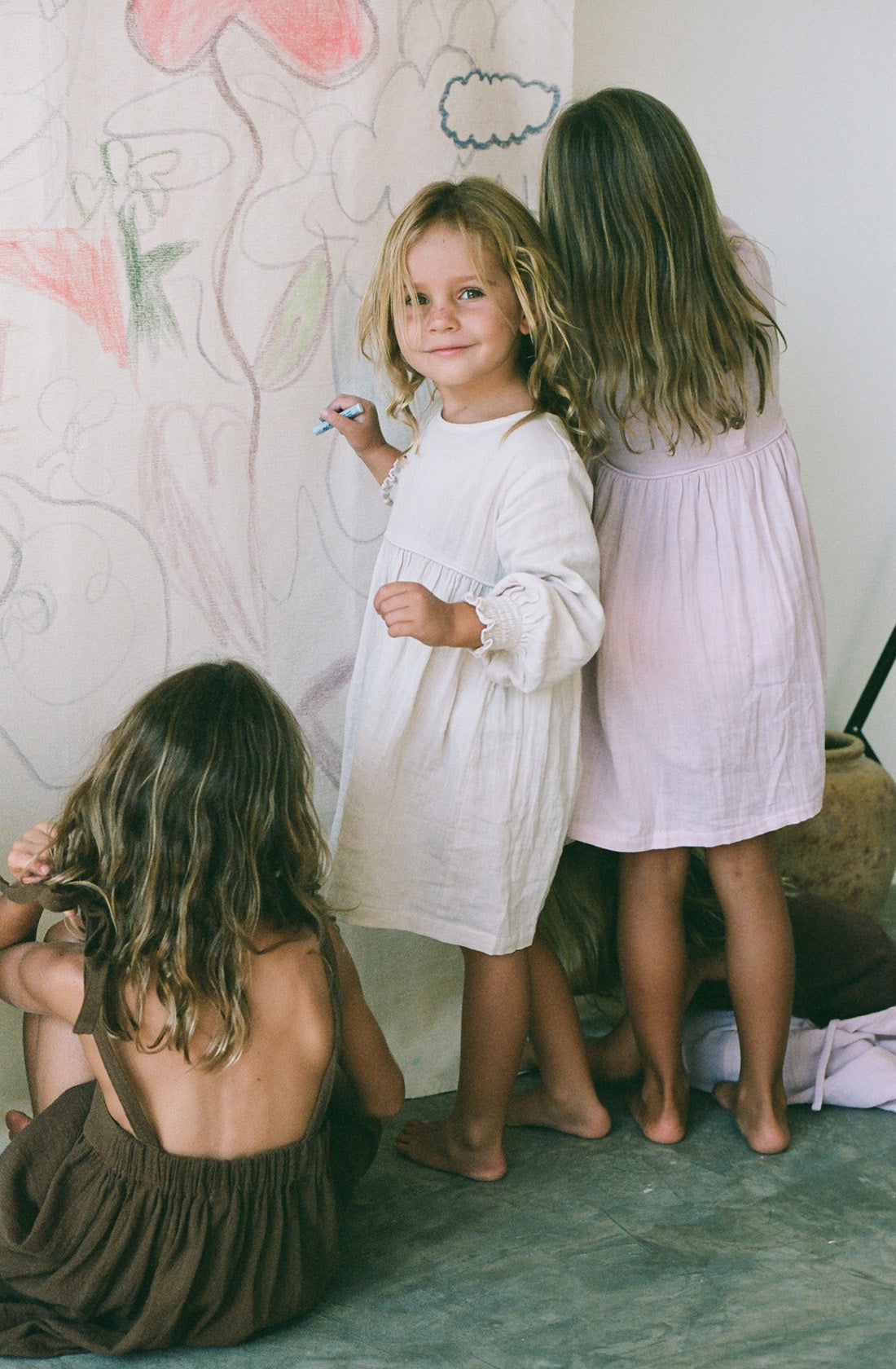 Young girl wearing the yumi dress in natural while drawing on a canvas.