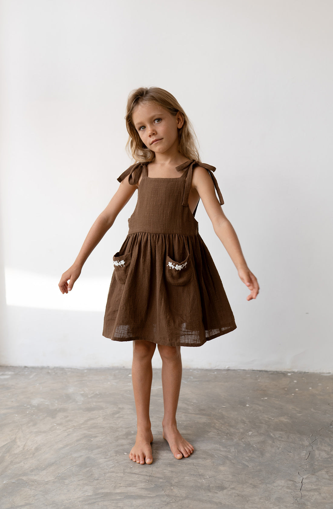 Young girl wearing the luna pinafore in cocoa.