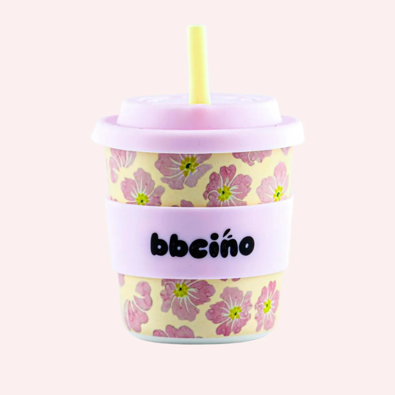 A 240ml Reusable BambinoCino cup from BBCINO, featuring a pastel pink lid and a yellow silicone straw. The cup is adorned with pink floral patterns and includes a pink sleeve with "bbeíbño" written in black text, set against a plain light pink background.