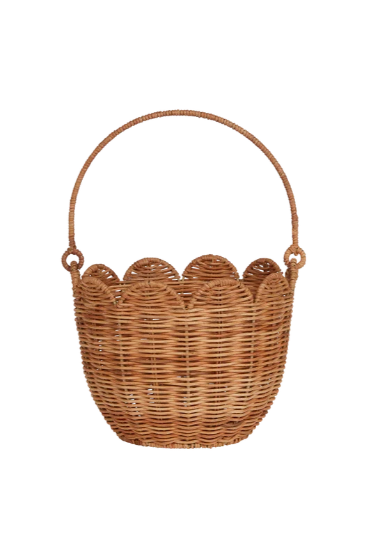 The Rattan Tulip Carry Basket Natural by OLLI ELLA is a medium-sized basket featuring a scalloped rim and a sturdy arched handle. This heirloom quality basket is handwoven with natural rattan in a traditional woven pattern, offering an empty interior.