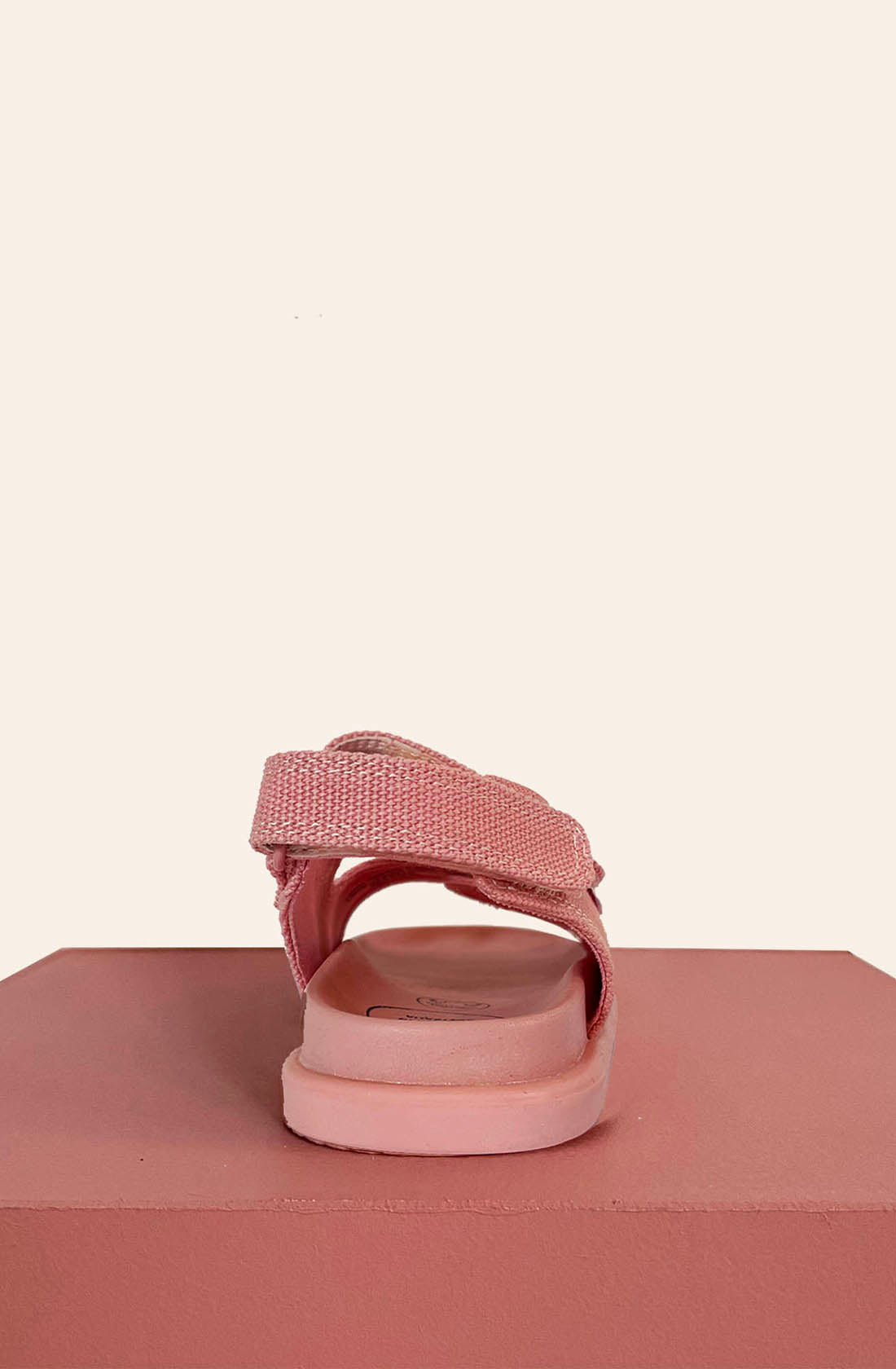 The PRE-ORDER Original Sandals Pink from PICCOLINI are displayed as a single sandal with a velcro strap, positioned on a pink platform against a light beige background. The rear view emphasizes its podiatrist-recommended design and non-slip rubber sole, ensuring optimal comfort and stability.