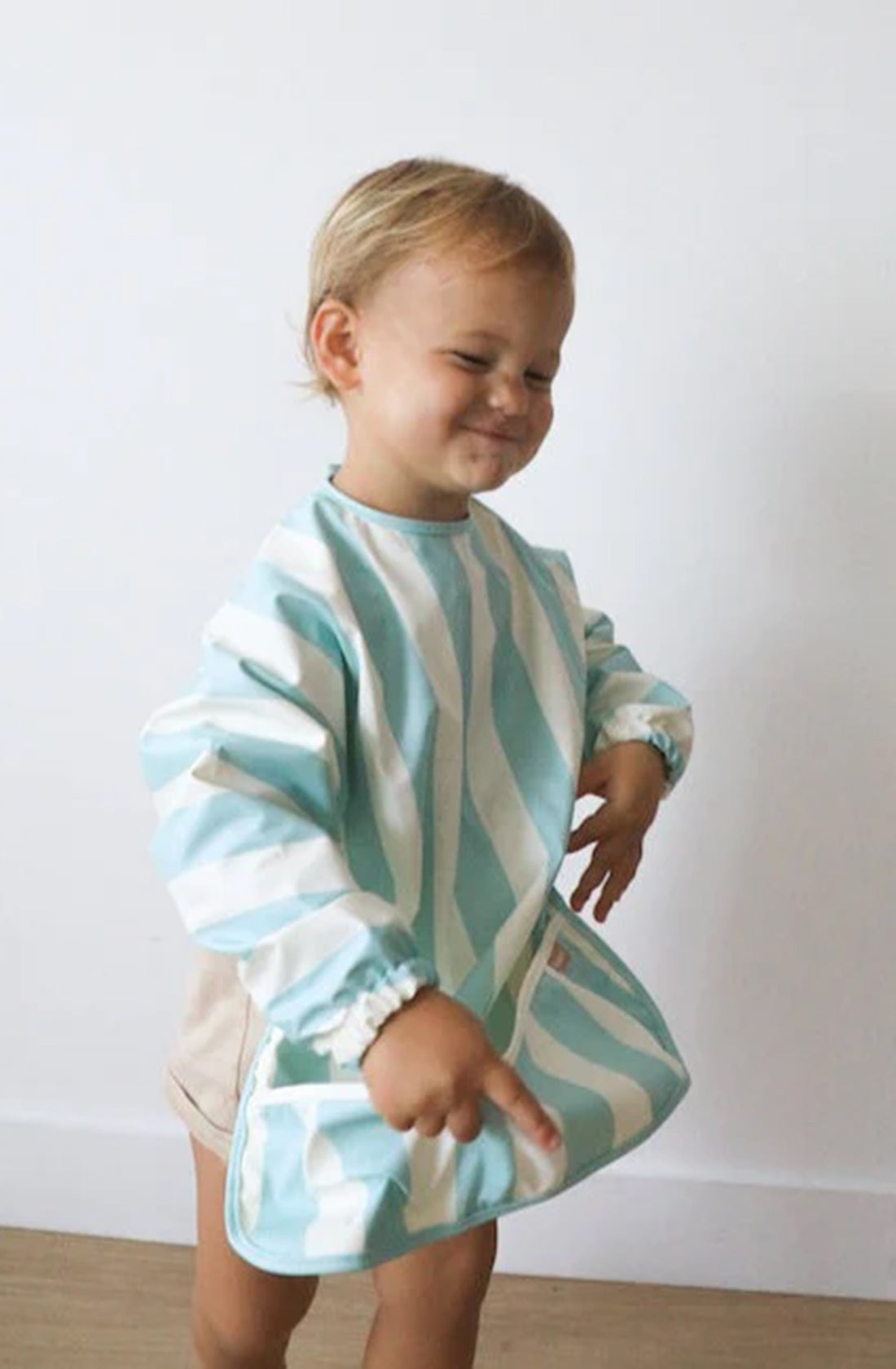 A young boy wearing the ROMMER Smock Bib in Sea Mist Stripe.