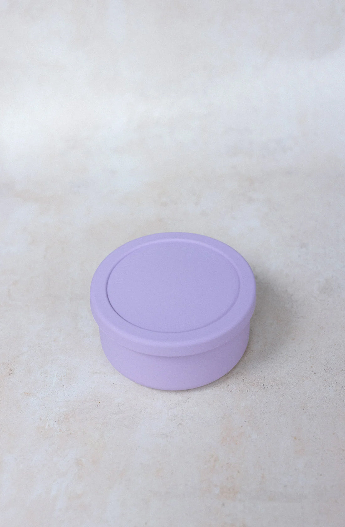 A Round Silicone Container Large (700ml) by THE WHOLESOME STORE, in lavender and BPA-free, with a flat lid, sits on a light beige surface.