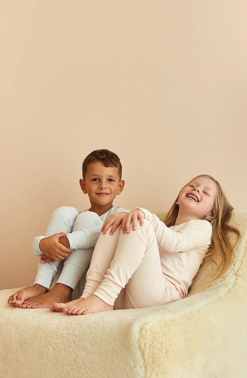 Girl and boy sitting on sheepskin couch wearing sleep sets in arctic blue and shell