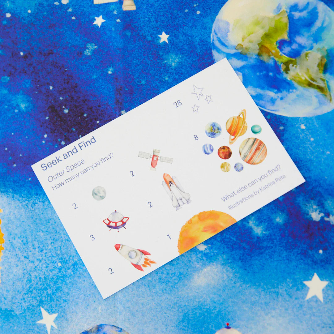 A vibrant Outer Space Seek & Find Playsilk game card from SARAH'S SILKS is displayed against a blue background. It includes illustrations of planets, a rocket, and a satellite with the prompt, "Seek and Find: Outer Space. How many can you find?" Various celestial objects encourage open-ended play alongside numbers.