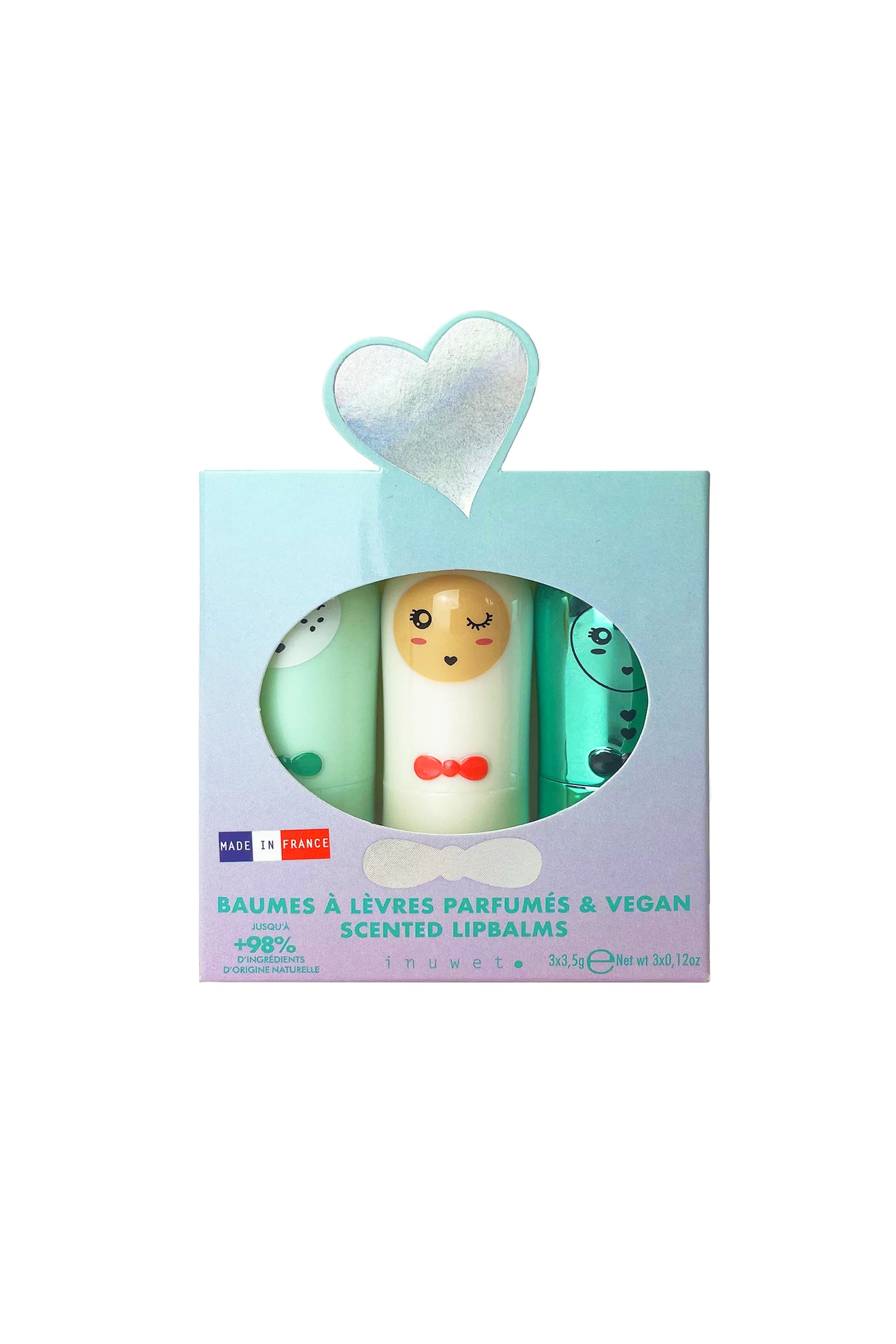 The Lip Balm Trio Seashell by INUWET comes in a boxed set of three scented lip balms, packaged with a heart-shaped window. The packaging displays "Made in France" and boasts that the product contains "98% ingredients of natural origin," including nourishing shea butter. The set includes white, yellow, and teal-colored tubes adorned with cartoon faces, each offering a delightful vanilla-coconut scent.