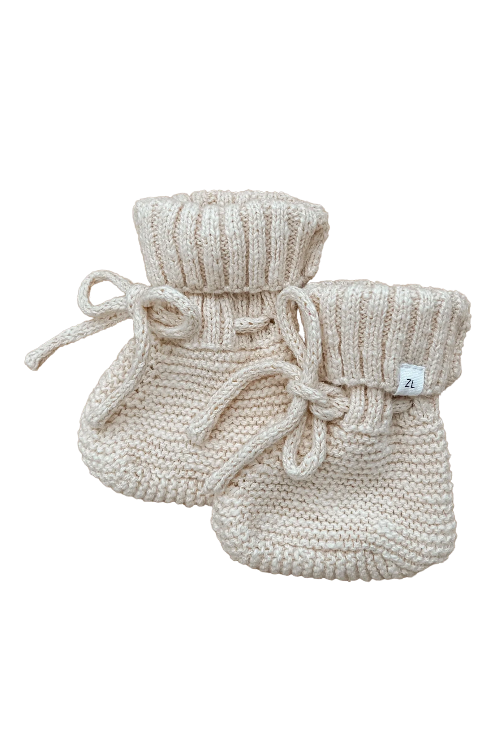 A pair of ZIGGY LOU's Booties Honey, beige knitted baby booties with ribbed cuffs and small bow ties, made from 100% textured cotton. Each bootie features a white label on the side with "2L" printed on it. The black background makes these heirloom pieces stand out clearly.