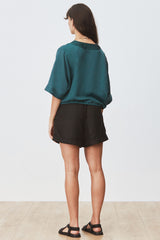 Rear view of woman wearing Eda Blouse in Seagrass with black shorts