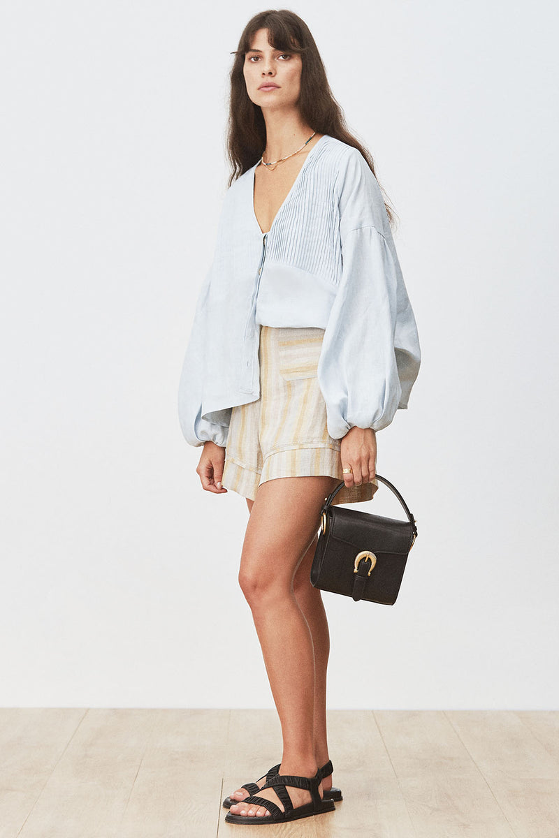 Woman wearing Eline Blouse in Celestial Blue tucked into striped shorts and holding a black bag