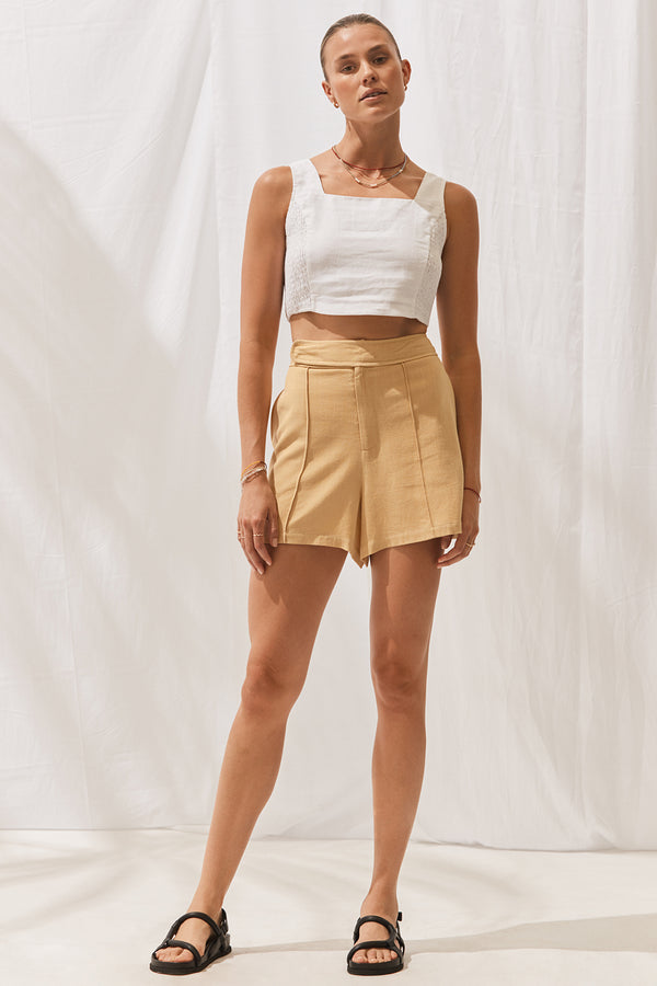 Woman wearing Kiki Shorts in Saffron with cropped white top. Full length, front view.