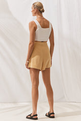 Woman wearing Kiki Shorts in Saffron with cropped white top. Full length, rear view.