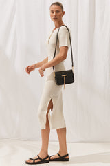 Woman wearing Isabella Dress in Off White with black handbag. Full length, side view.