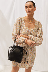 Woman wearing Mariia Dress in Luzianes Floral with black handbag. Close up, front view.