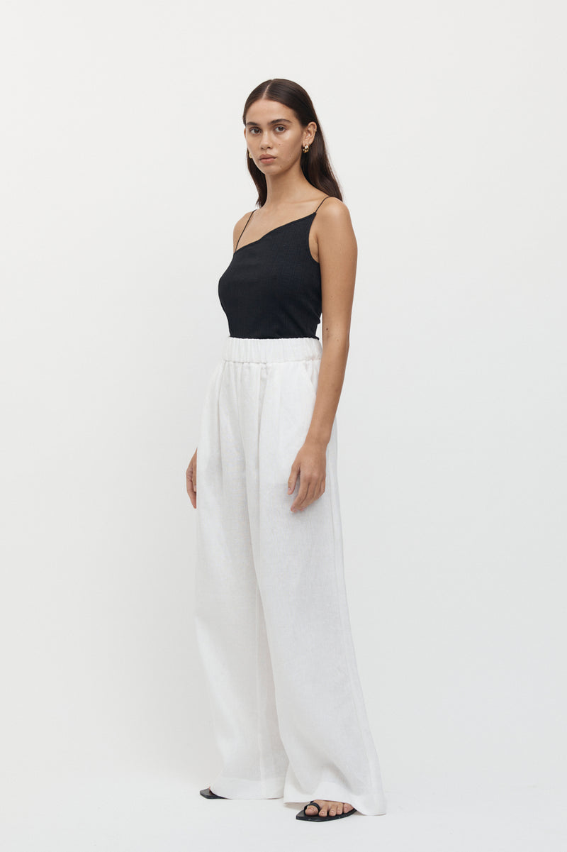 Side view of woman wearing Sete Linen Elastic Waist Pant in white with an asymmetrical black top.