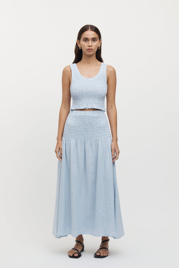 Full length view of woman wearing Eze Shirred Linen Midi Skirt in sky, with matching crop top.