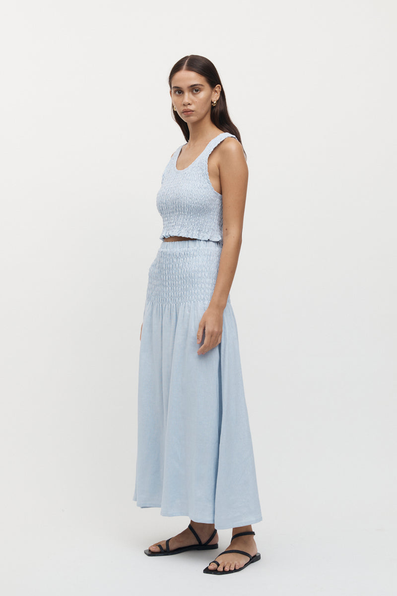 Side view of woman wearing Eze Shirred Linen Midi Skirt in sky, with matching crop top.