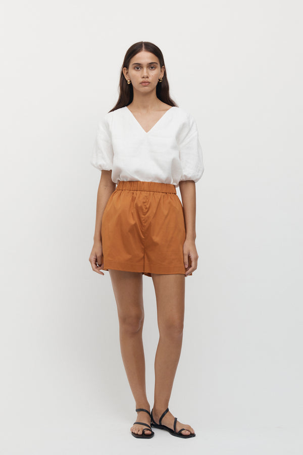 Full length view of woman wearing Giverny Puff Sleeve Top in white with burnt orange shorts.