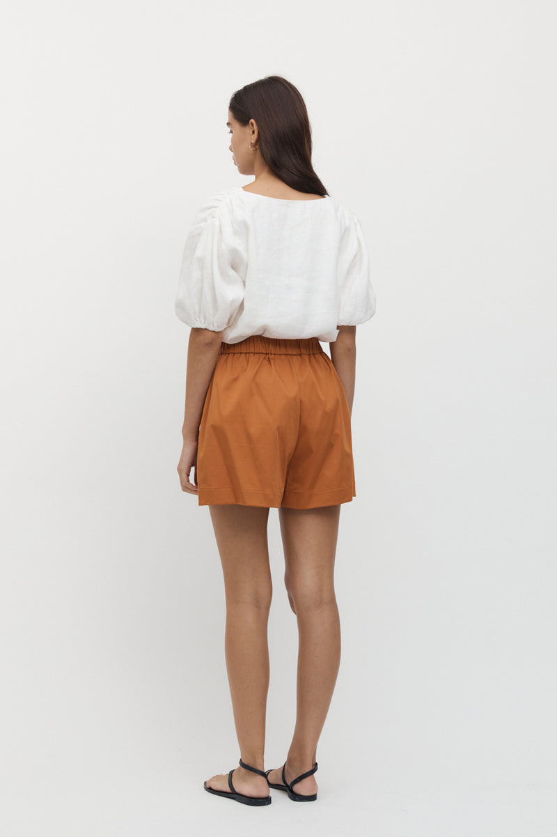 Rear view of woman wearing Giverny Puff Sleeve Top in white with burnt orange shorts.
