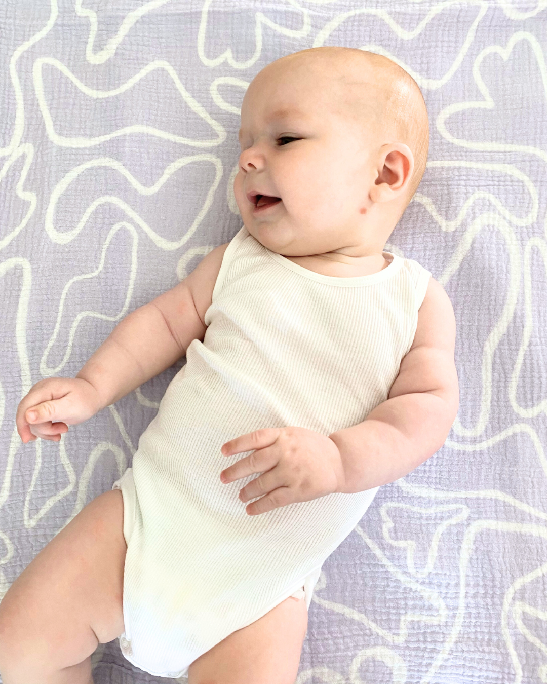 A baby wearing the laze 100% organic cotton swaddle in lilac colour.