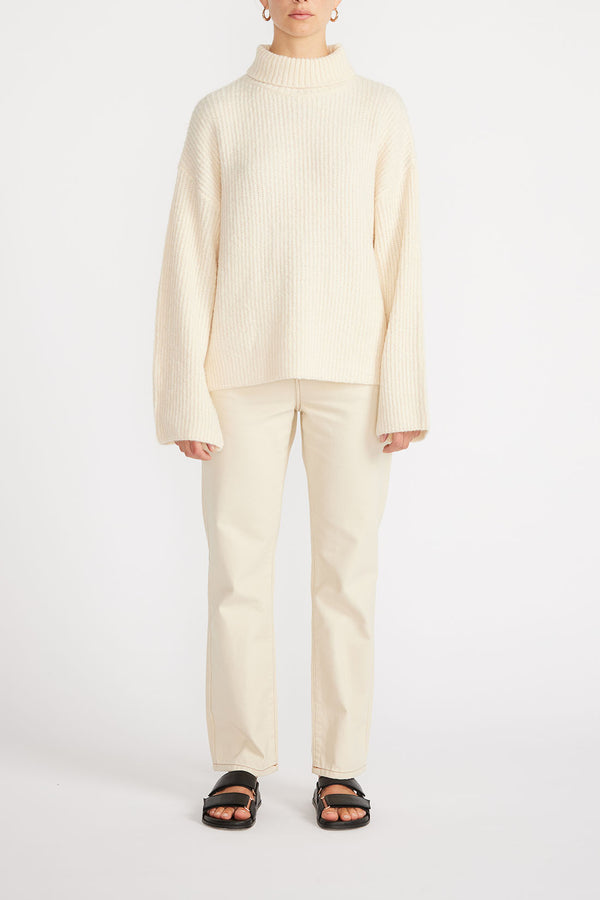Front view of woman wearing Esme Roll Neck Jumper in cream with cream jeans