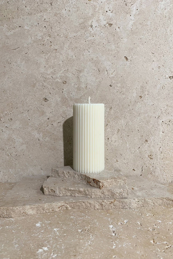 Ribbed pillar candle cream on stack of travertine